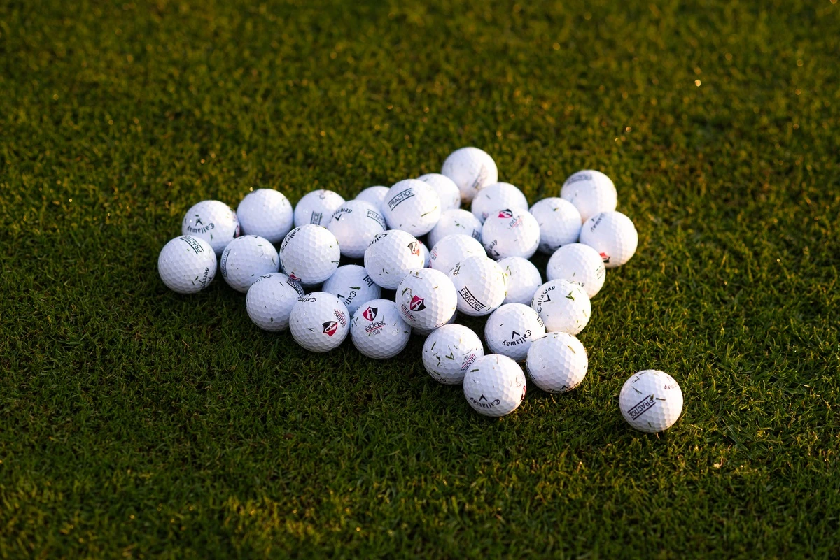 Montón de pelotas de golf blancas sobre el césped del campo de práctica, iluminadas por la luz cálida del atardecer