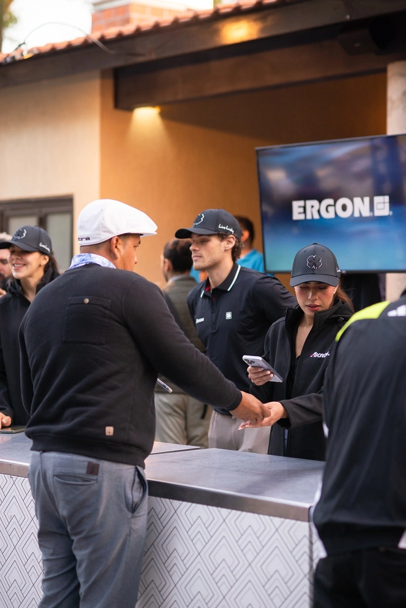 Personal del evento atendiendo a un jugador en el módulo de registro, mientras revisan información en el teléfono y saludan a los participantes.