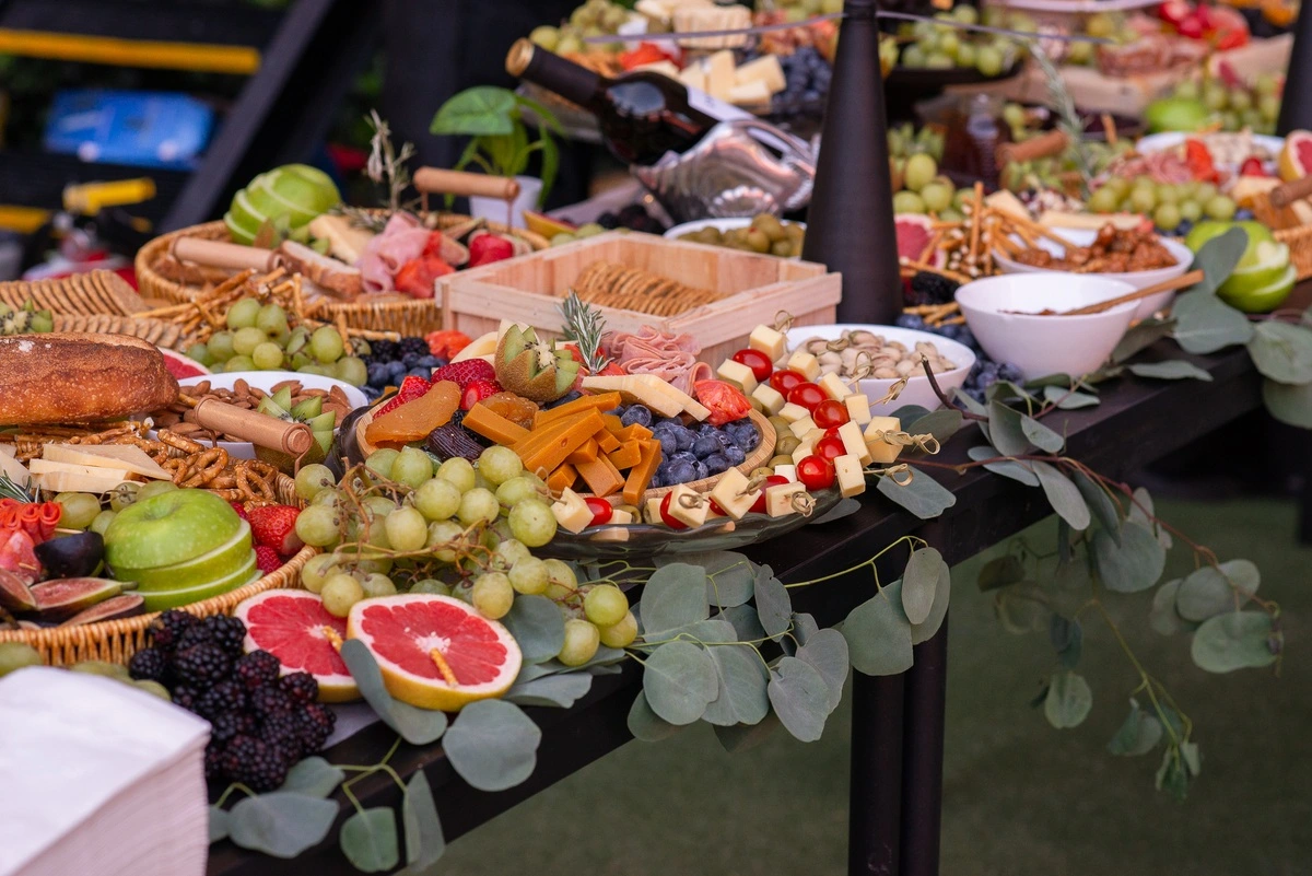 Mesa con frutas, quesos, pan y charcutería decorada con hojas y variedad de bocadillos.
