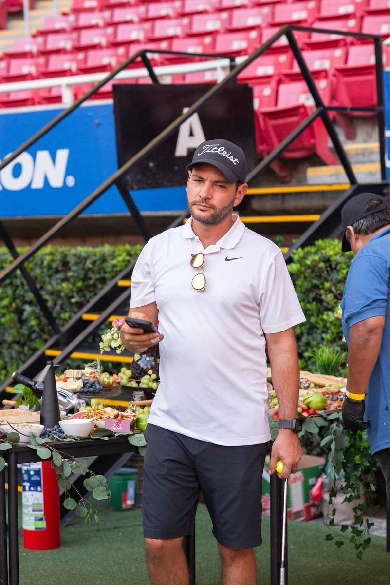 Hombre con ropa de golf usando su celular frente a una mesa con frutas y bocadillos.