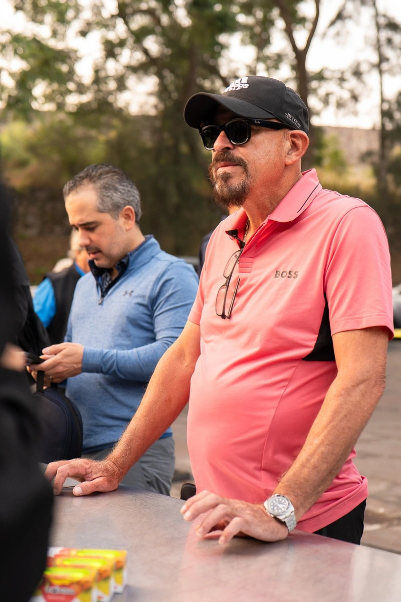 Hombre con polo rosa y gafas oscuras esperando en el módulo de registro del evento de golf.
