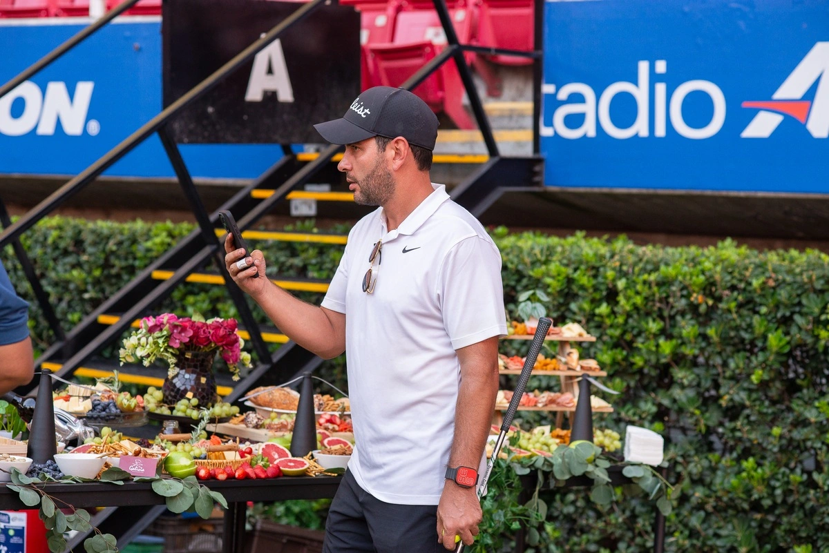 Hombre con ropa de golf usando su celular frente a una mesa de buffet con frutas y bocadillos