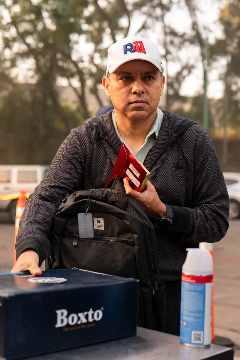 Hombre con gorra blanca sosteniendo su kit del torneo junto a una mochila sobre la mesa
