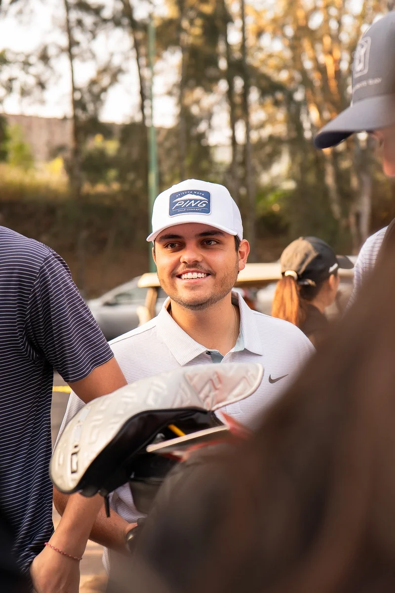 Jugador con gorra blanca sonríe mientras sostiene su equipo durante el registro del torneo
