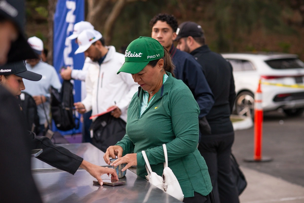 Mujer con gorra verde realizando su registro en el evento de golf frente al módulo de atención.
