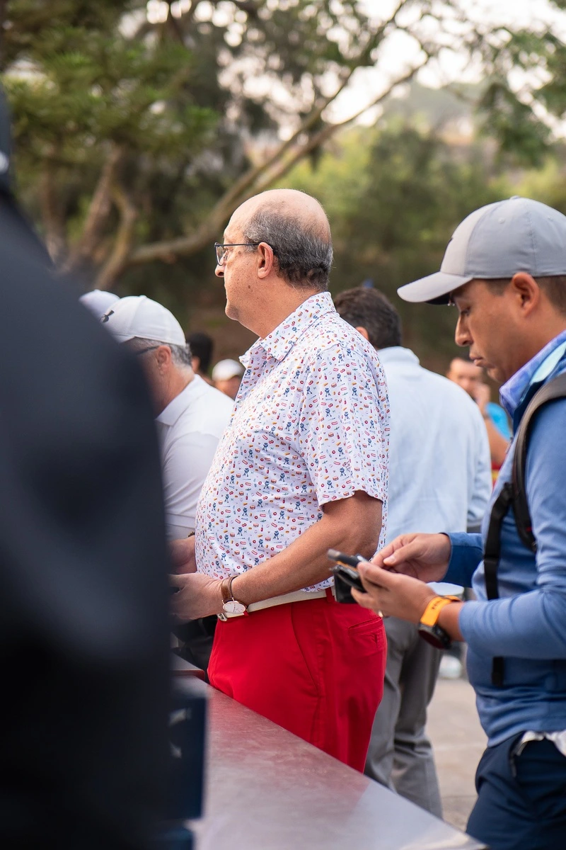 Hombre con camisa estampada y pantalón rojo esperando en la fila de registro del torneo