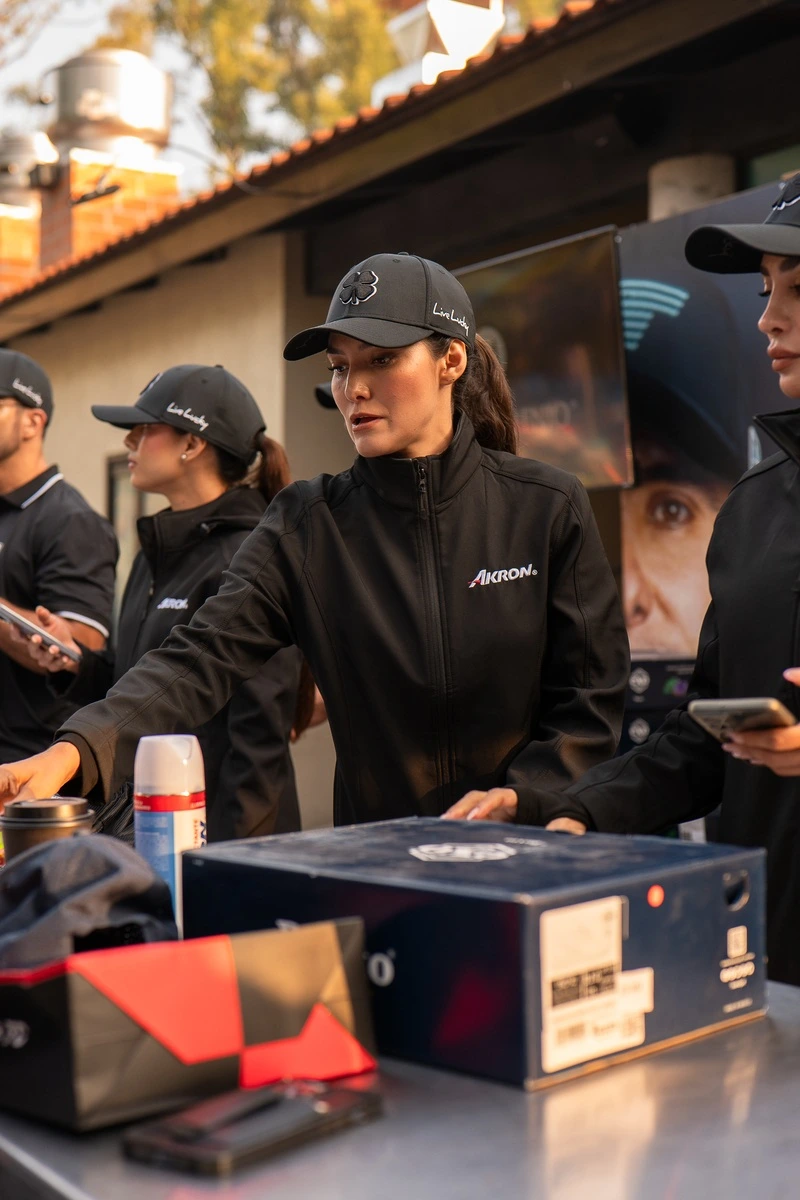 Mujer del staff entregando kits del torneo en el módulo de registro, rodeada de compañeras.