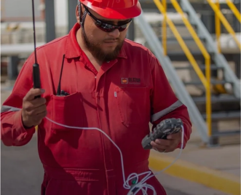 Supervisor con uniforme rojo y equipo de seguridad sosteniendo cables de comunicación en sitio industrial.