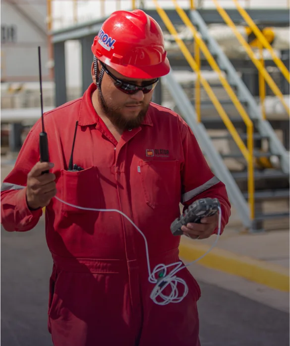 Supervisor con uniforme rojo y equipo de seguridad sosteniendo cables de comunicación en sitio industrial.