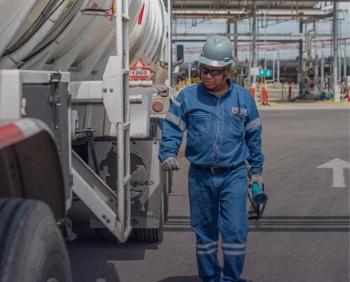 Técnico con equipo de seguridad inspeccionando camión cisterna en sitio industrial.