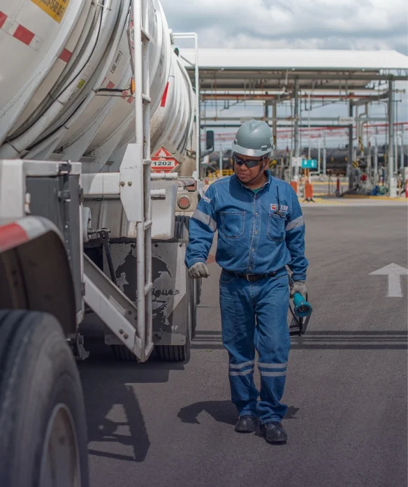 Técnico con equipo de seguridad inspeccionando camión cisterna en sitio industrial.