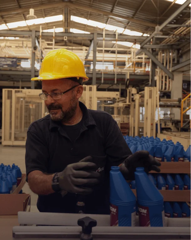 Trabajador con equipo de seguridad inspeccionando botellas de producto químico en línea de producción.